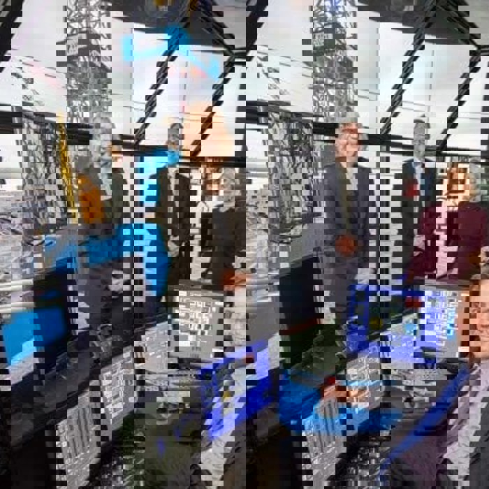 Four people are in a high-tech control room with several monitors displaying offshore drilling equipment. One person is seated, operating the controls, while the others stand behind, observing.