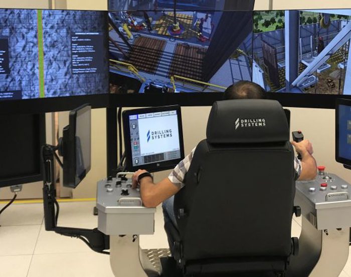 Person operating a drilling simulator with multiple screens and control panels.