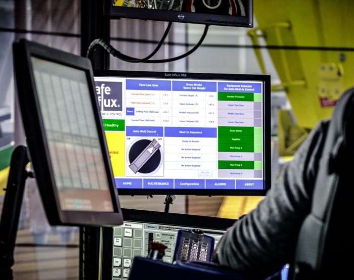 A worker operates machinery using multiple screens displaying data and controls in an industrial setting.