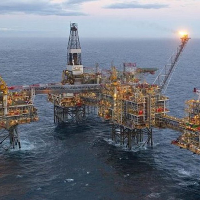 An offshore oil platform with multiple interconnected structures, surrounded by ocean water, under a partly cloudy sky.