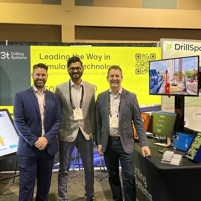 Three men in suits stand in front of an exhibition booth featuring cutting-edge technology displays and promotional banners, emphasizing innovative training solutions.
