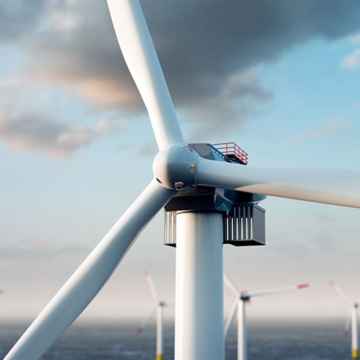 Close-up of a wind turbine with large blades against a cloudy sky, with more turbines visible in the background over the ocean.