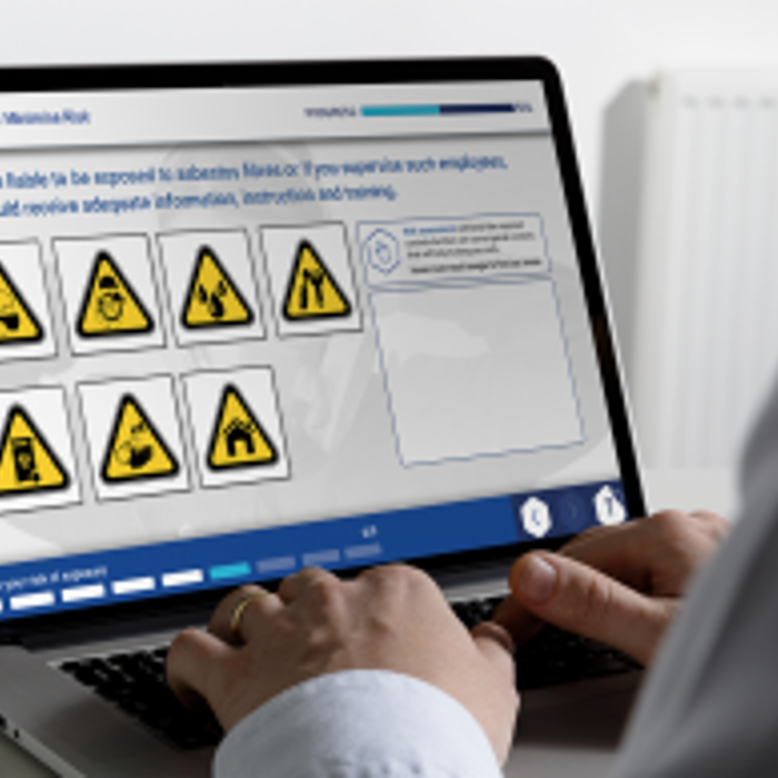 A person using a laptop showing a safety training module with various warning symbols displayed on the screen.