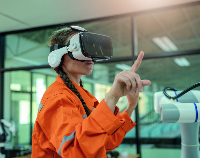 A person wearing an orange jacket and VR headset interacts with a robotic device in a modern industrial setting.
