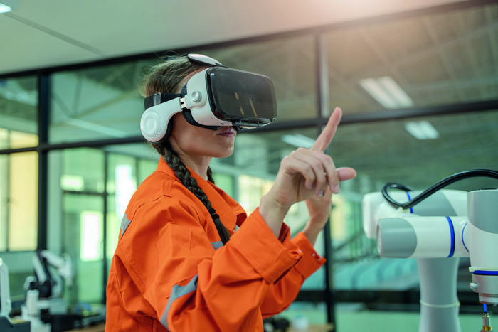 A person wearing an orange jacket and VR headset interacts with a robotic device in a modern industrial setting.