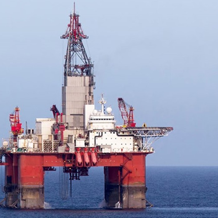 An offshore oil rig stationed in the ocean, with red and white machinery and equipment visible against a clear sky.
