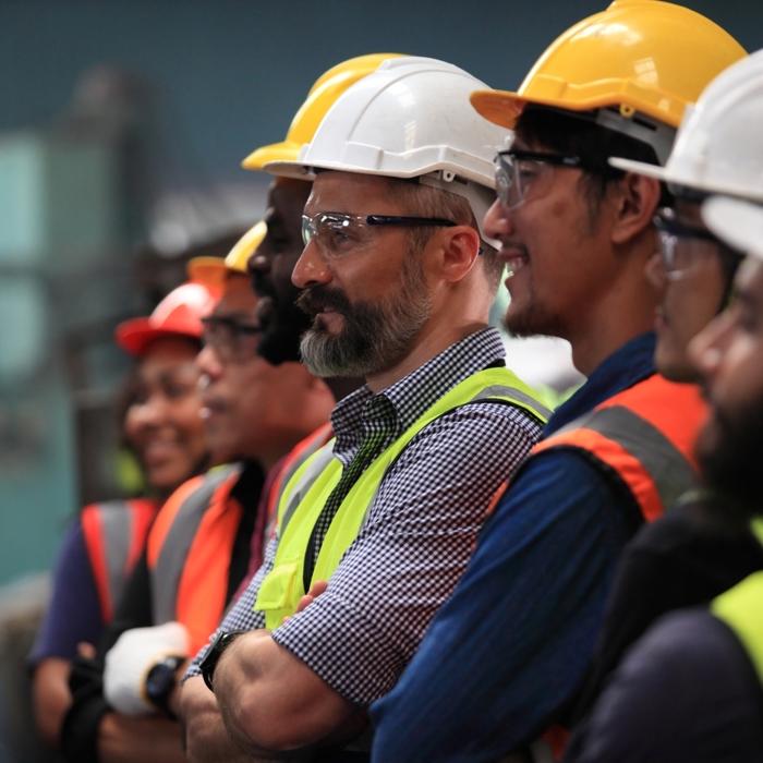 A group of workers wearing safety helmets and vests stands together, focusing intently on a training exercise just out of view.