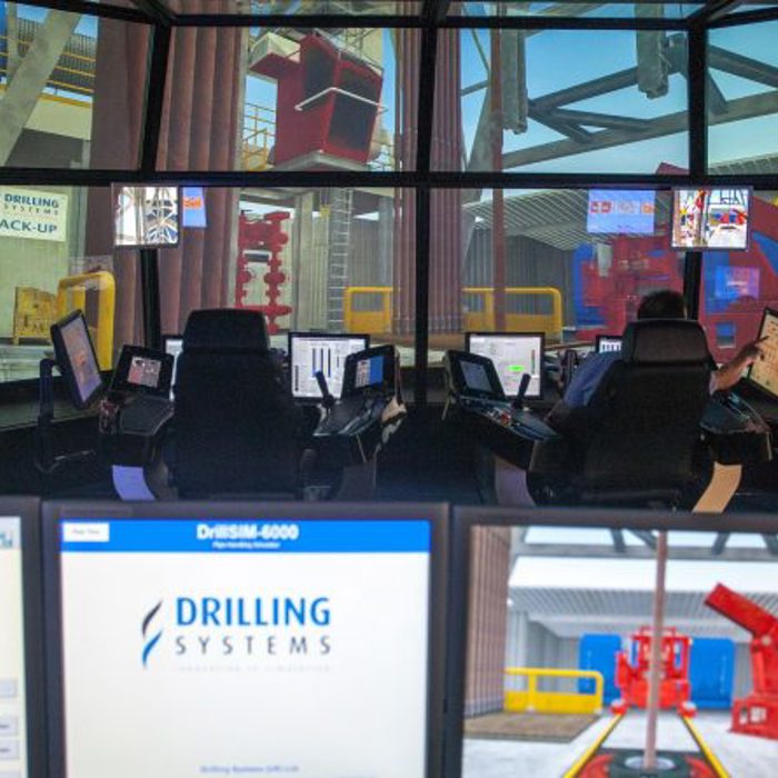 Two operators sit in a control room using advanced simulation software from Drilling Systems to manage virtual oil and gas drilling operations displayed on multiple screens.