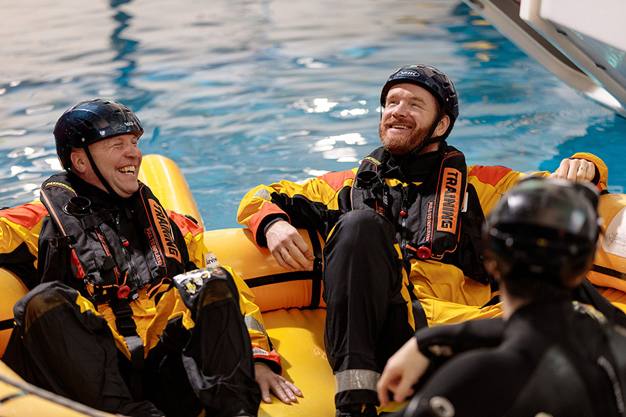 People wearing protective suits and helmets sit in an inflatable raft in a pool, honing their skills during a training exercise.