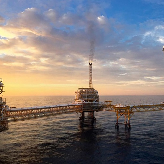 An offshore oil platform at sunset with a network of connected walkways over the ocean and a crane on the right side.
