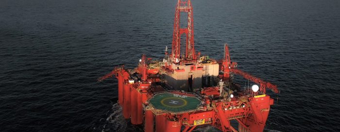 A red offshore oil drilling platform is positioned in open water, displaying a helipad and various equipment on its deck.