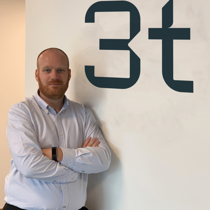 Jamie stands with arms crossed next to a wall displaying the letters "3t".