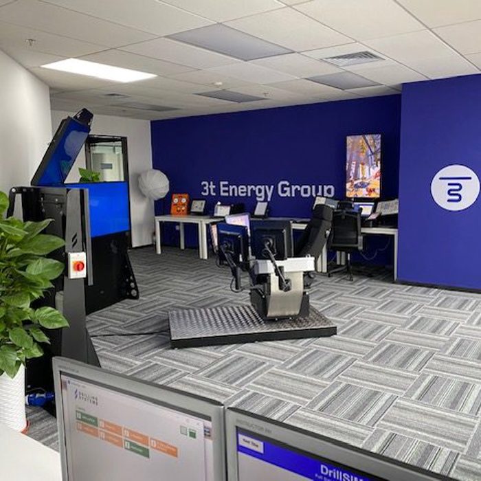 An office with a blue and white color scheme features the 3t Energy Group logo, several desks with computers, a plant, and specialized equipment in the foreground.