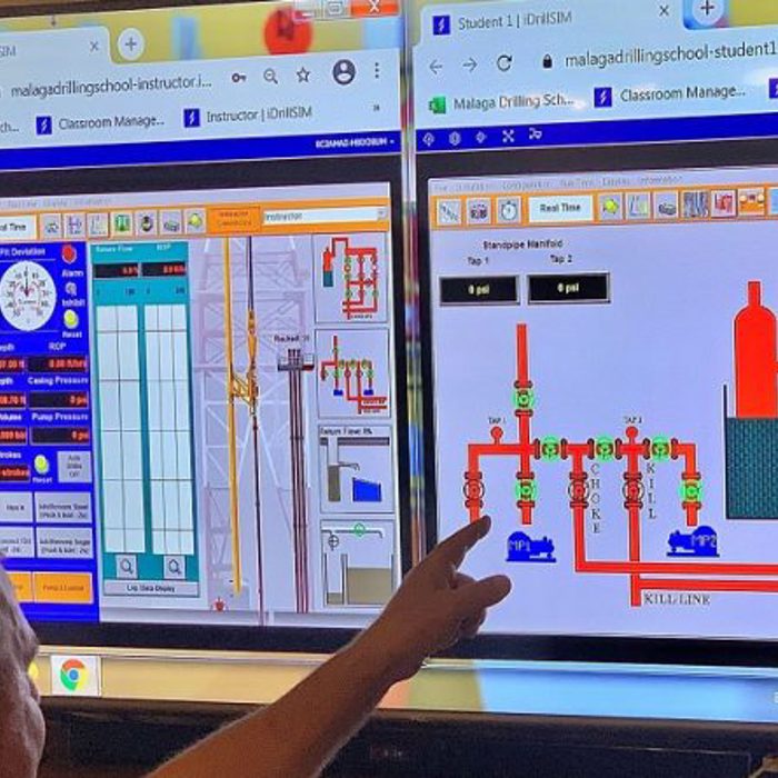 A person points at two computer screens displaying detailed diagrams and controls, seemingly related to a technical or industrial application.