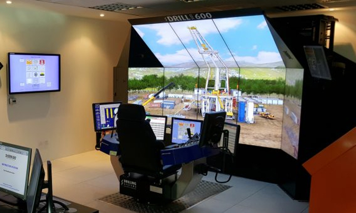 A modern drilling simulator setup with multiple screens showing an outdoor drilling scenario. The control console is equipped with joysticks and monitors displaying various operational data.