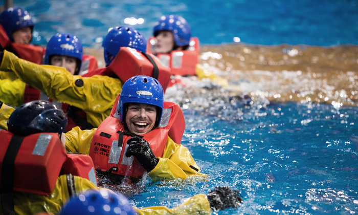 Individuals wearing life vests and helmets participate in water safety training, smiling and interacting in a pool.