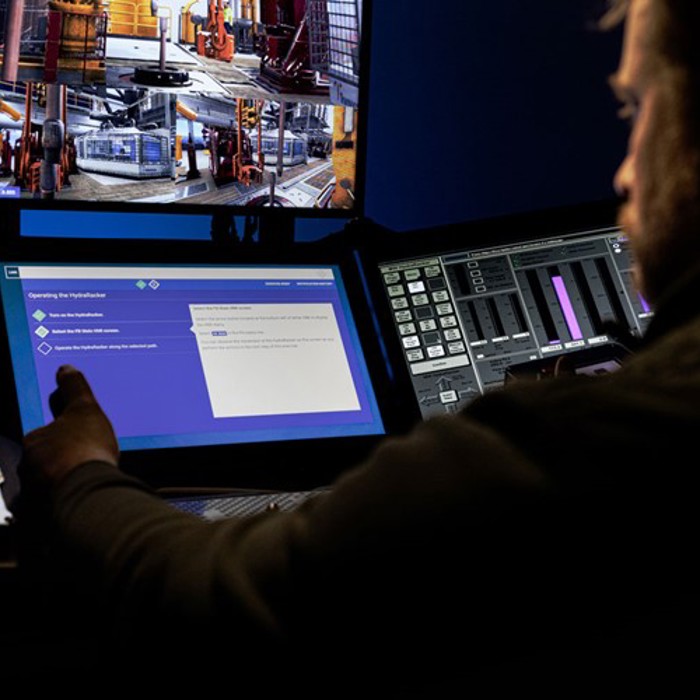 A person operates equipment using various screens, including one showing images of machinery and another displaying digital data and controls.