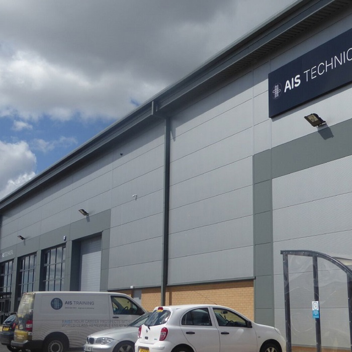 Outdoor view of AIS Technical building with parked cars in front. The structure has large doors and signs indicating the company's name. Cloudy sky overhead.
